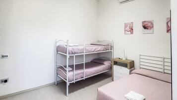 Ein Stockbett mit Schreibtisch und Stuhl, ein Nachttisch mit Lampe sowie drei an der Wand hängende Blumenbilder.