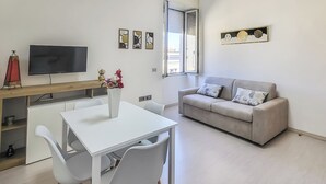 Ein modernes Wohnzimmer mit Fernseher, Esstisch mit Stühlen, einer Couch mit Kissen und Bildern an den Wänden.