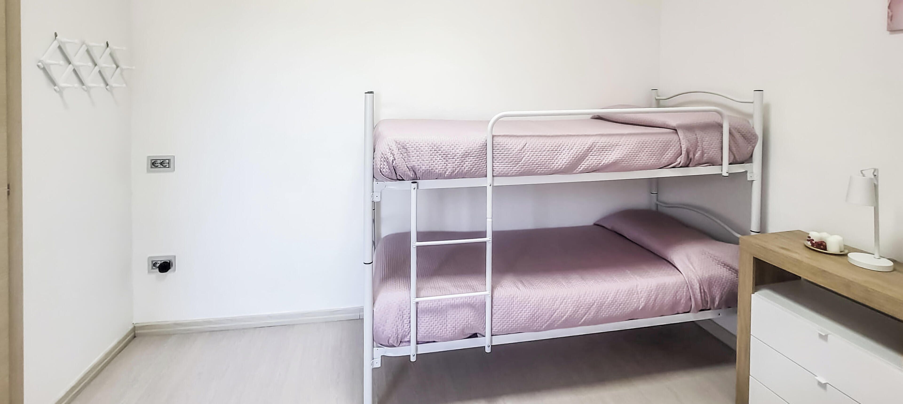 Un llit superposat amb escala, un escriptori amb làmpada i un interruptor de llum fixat a la paret.