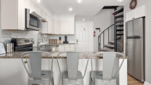 A modern kitchen with white cabinets, stainless steel appliances, and a central island with bar stools. - Great Location for Sunday Fireworks and Easy Walk to the Beach! Has a Pool! (Ocean City)