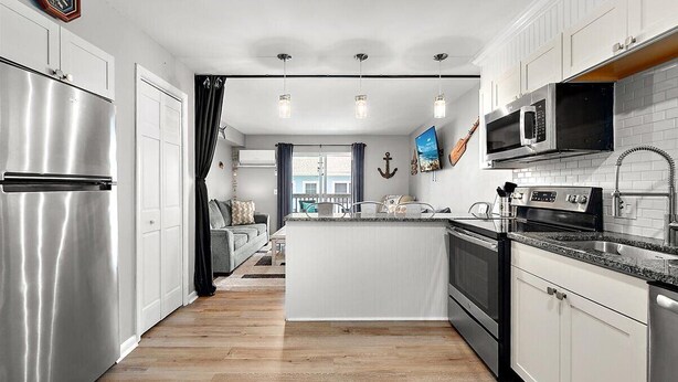 A modern kitchen with a central island, stainless steel appliances, and a view to a balcony. - Great Location for Sunday Fireworks and Easy Walk to the Beach! Has a Pool! (Ocean City)