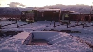 Ein verschneiter Außenbereich mit einer Holzhütte und einer Metallbank.