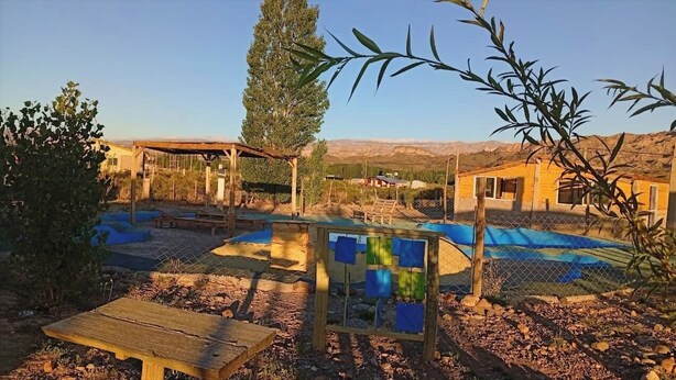 Ein rustikaler Außenbereich mit Holztisch, überdachter Sitzgelegenheit und Schwimmbecken.