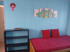 Una habitación con pared azul, cama con ropa de cama roja, mesita de noche de madera con una cesta y un adorno en la pared.