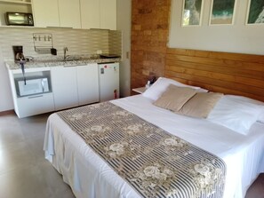 Un dormitorio con cama, cabecera de madera, zona de cocina con refrigerador y microondas.