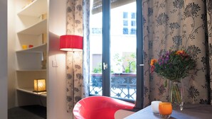 A room with a red chair, a table with a vase of flowers, a lamp, and a view through a window with a balcony. - Marvelous 2-bedroom apartment in Paris perfect for your getaway (Paris)