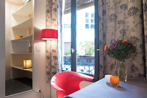 A room with a red chair, a table with a vase of flowers, a lamp, and a view through a window with a balcony. - Marvelous 2-bedroom apartment in Paris perfect for your getaway (Paris)