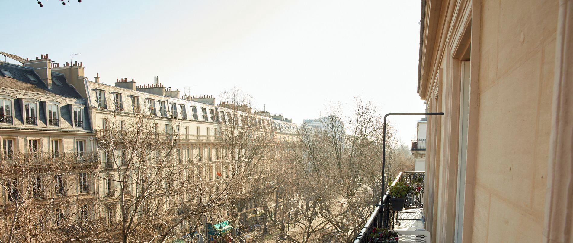 A row of European-style buildings with balconies, a clear sky, and leafless trees.