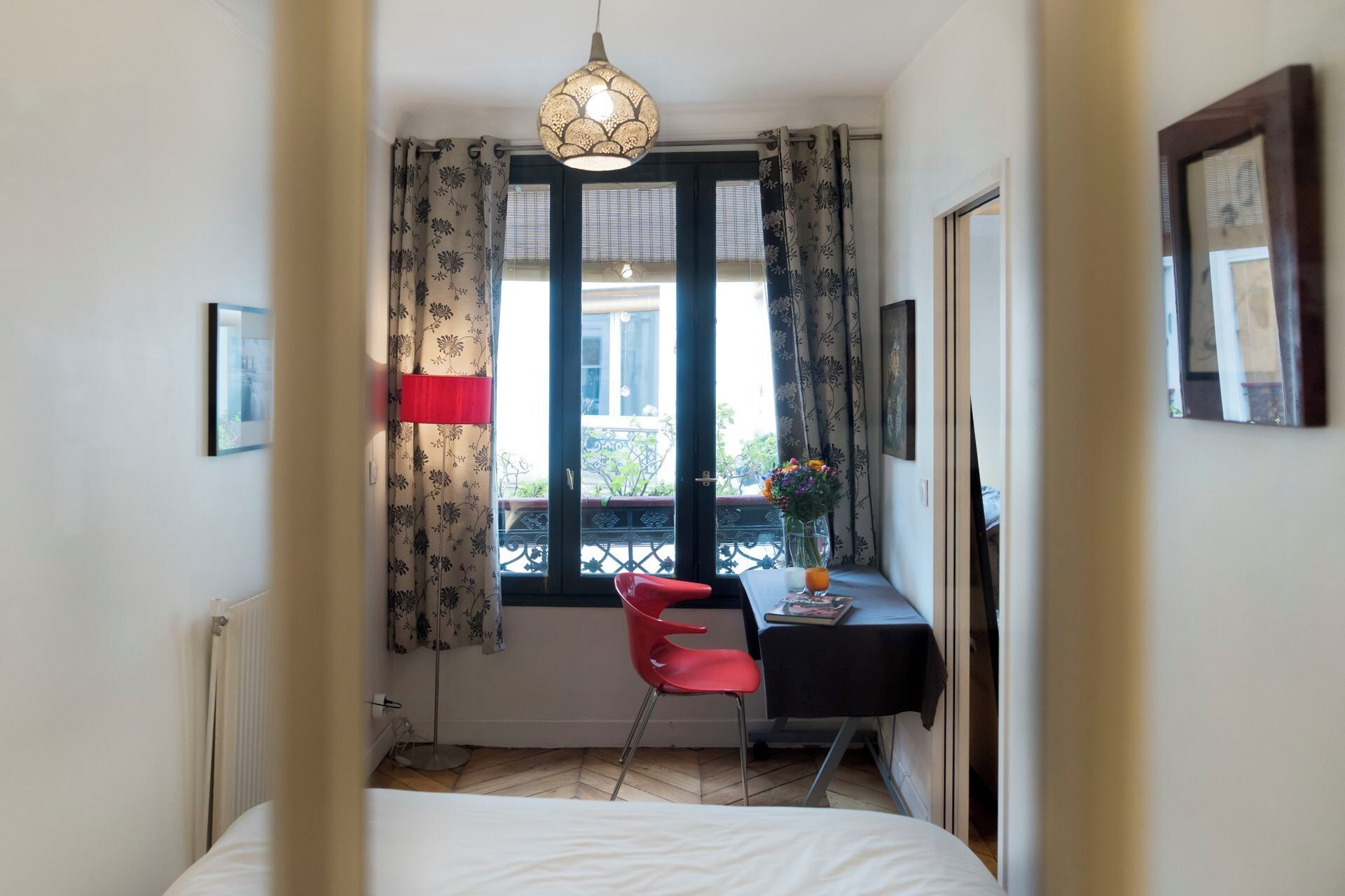 Un dormitorio con cama, escritorio y silla, ventana con cortinas, radiador y lámpara colgante.