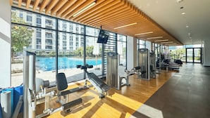 A gym with exercise equipment, large windows, and a view of a swimming pool. - PVH - Executive Residences 2BR (Dubai)