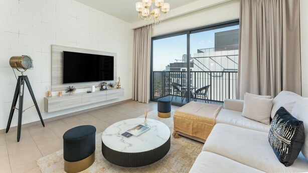 A modern living room with a flat-screen TV, a round coffee table, a sofa, and a balcony with outdoor seating. - PVH - Executive Residences 2BR (Dubai)