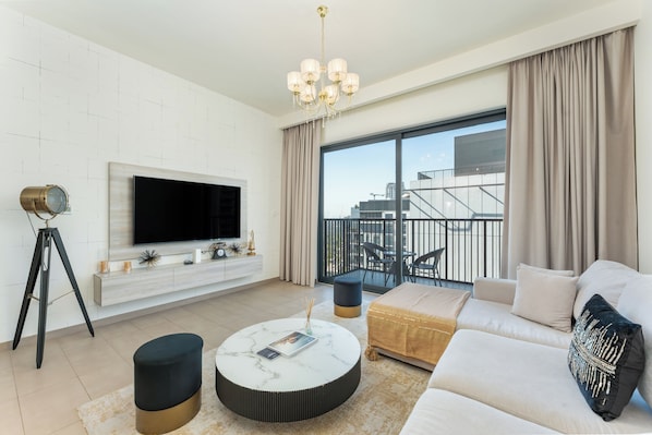 Ein modernes Wohnzimmer mit Flachbildfernseher, rundem Couchtisch, einer Couch und einem Balkon mit Sitzgelegenheit.