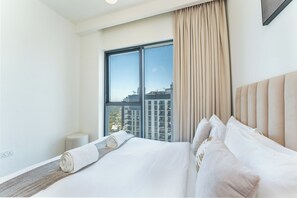 Ein Hotelzimmer mit großem Fenster, einem Bett mit weißer Bettwäsche, einem Kopfteil und einem kleinen Nachttisch.