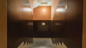 A hallway with a dark brown wall, a light brown ceiling, and a tiled floor. - Hotel Shiri Krishna  (Mathura)