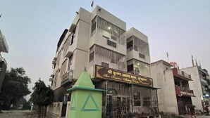 A multi-story building with a sign in a foreign language, a green structure with a triangular design, and a clear sky. - Hotel Shiri Krishna  (Mathura)