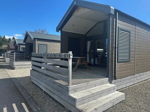 A small, single-story cabin with a covered porch, a wooden fence, and a gravel driveway. - Self-catering Lodge Inverness - Sleeps 4 (Inverness)