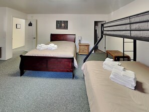 Une chambre à coucher avec un lit en bois, un lit superposé, une petite table de chevet, une lampe et un tableau encadré au mur.
