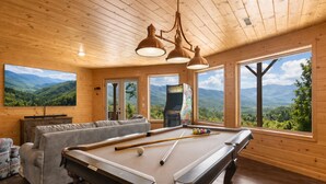 Ein Billardtisch in einem Raum mit Holzwänden und großen Fenstern mit Blick auf die Berge.