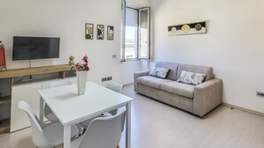 A modern living room with a white table and chairs, a beige sofa with patterned cushions, a flat-screen TV, and artwork on the walls. - Dolia Court - Dolianova (Dolianova)