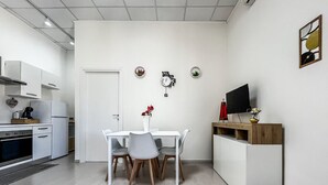 A modern kitchen with white cabinetry, a dining table with chairs, a TV on a wooden stand, and a small potted plant on the wall. - Dolia Court - Dolianova (Dolianova)