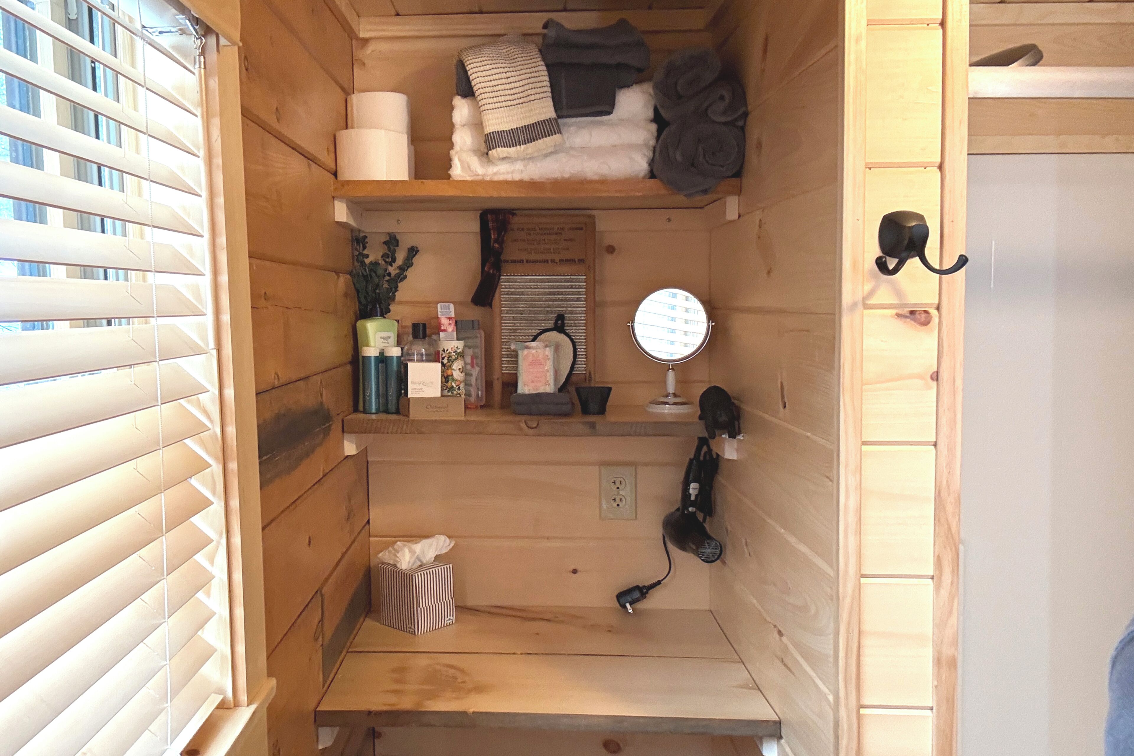A wooden room with a shelf holding towels, a mirror, and toiletries.