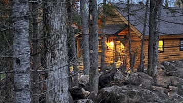 Une cabane en rondins entourée d’arbres et de rochers.