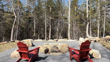 Deux chaises Adirondack rouges sont placées face à un foyer entouré de rochers, avec une forêt en arrière-plan.