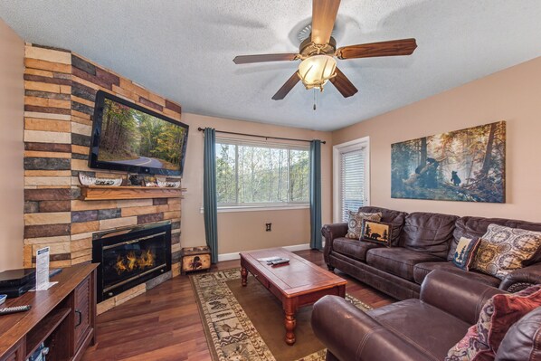 A living room with a fireplace, a television mounted on a stone wall, a ceiling fan, and a couch with decorative pillows. - Escape to the serene beauty of Gatlinburg with Mountain View Memories Unit #2102 (Gatlinburg)