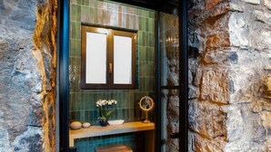 Une salle de bain avec un mur en pierre, un meuble-lavabo en bois, un miroir et un petit tabouret.