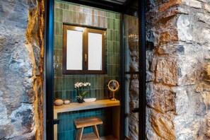 A bathroom with a stone wall, a wooden vanity, a mirror, and a small stool. - Loft 15 Torno Lake Como (TORNO)