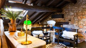 Une pièce rustique avec un plafond en bois, des murs en pierre, un banc en bois, une table avec une lampe et une plante.