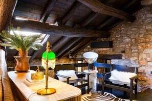 A rustic room with a wooden ceiling, stone walls, a wooden bench, a table with a lamp, and a plant. - Loft 15 Torno Lake Como (TORNO)