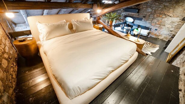 Une chambre dotée d’un grand lit, de poutres en bois, de murs en pierre et d’une atmosphère rustique.