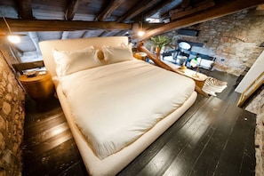 Ein Schlafzimmer mit einem großen Bett, Holzbalken, Steinwänden und rustikalem Ambiente.