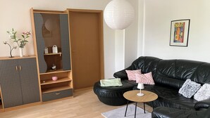 Ein modernes Wohnzimmer mit einer schwarzen Ledersofa, einem Holzkabinett mit Regalen, einem runden Couchtisch und einer Pendelleuchte.