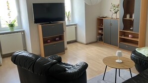 Ein modernes Wohnzimmer mit Flachbildfernseher, schwarzem Ledersofa, Holzausbau und einem kleinen runden Tisch.