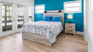 A bedroom with a bed, a nightstand, a ceiling fan, and a window. - Driftwood Beach House: Your Perfect Getaway in Matagorda (Matagorda)