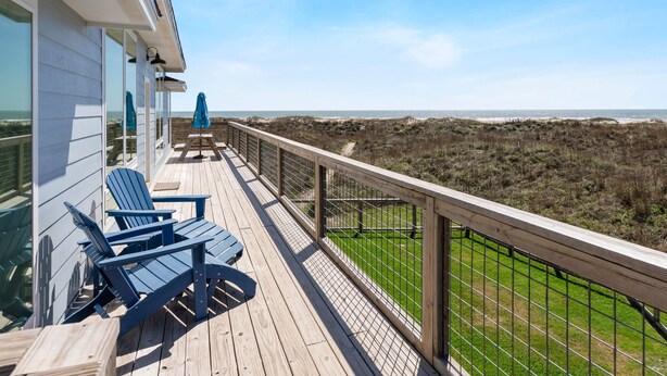 A wooden deck with two blue Adirondack chairs, a table, and a blue umbrella. - Driftwood Beach House: Your Perfect Getaway in Matagorda (Matagorda)