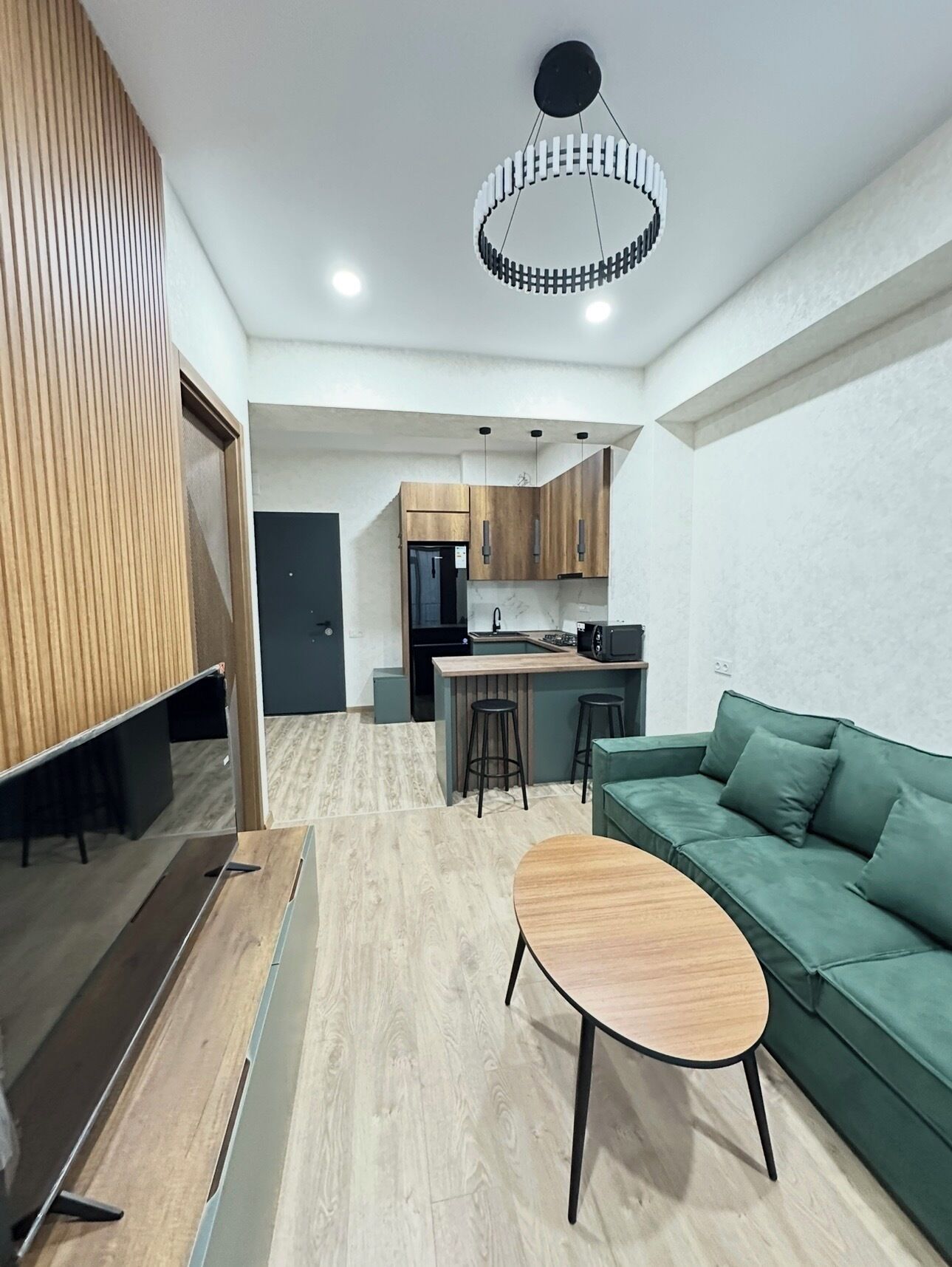 Una cocina moderna con armarios de madera, una isla central y un sofá verde en una sala de estar.