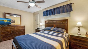 A bedroom with a bed, dresser, nightstand, lamp, ceiling fan, and a television on the dresser.