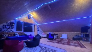 Ein Dachzimmer mit Holzboden, einem gemusterten Teppich, Sitzsäcken und einer blau beleuchteten Decke.