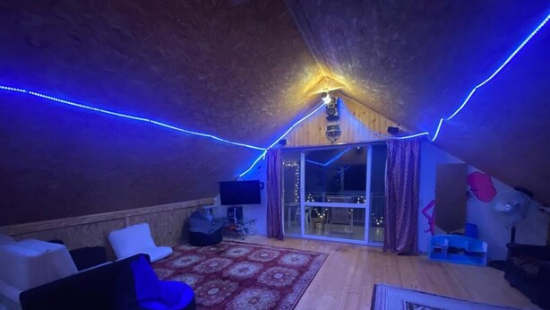 Ein Dachzimmer mit Holzboden, einem roten Teppich mit Muster, einem schwarzen Sitzsack, einem weißen Sofa und einem großen Fenster mit Vorhängen.