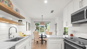 Een moderne keuken met witte kasten, een roestvrijstalen oven en een eethoek met een ronde tafel en stoelen.