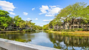 A calm river with buildings on either side, a clear sky, and a wooden bridge railing. - Stunning remodeled Turtle Cove (Kiawah Island)