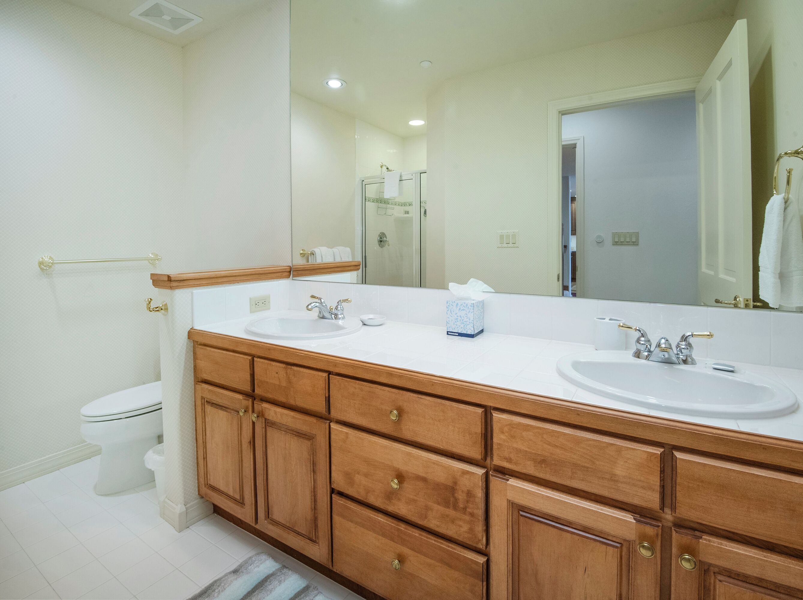 A bathroom with two sinks, a toilet, wooden cabinets, and a large mirror.