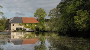 A stone building with a red roof by a calm water body, surrounded by lush greenery. - Moulin Moulin (Dannes)