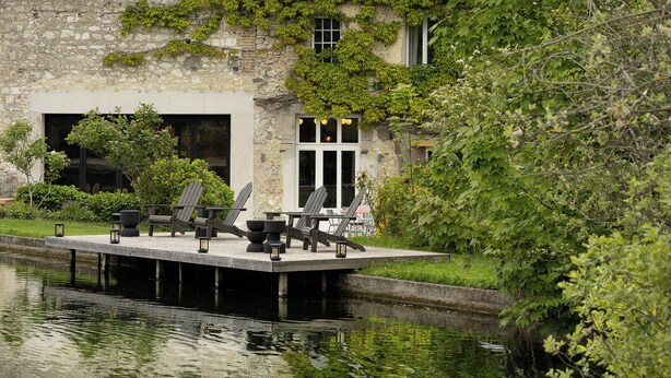 A dock with chairs and tables, a stone building with ivy, and a calm water body. - Moulin Moulin (Dannes)