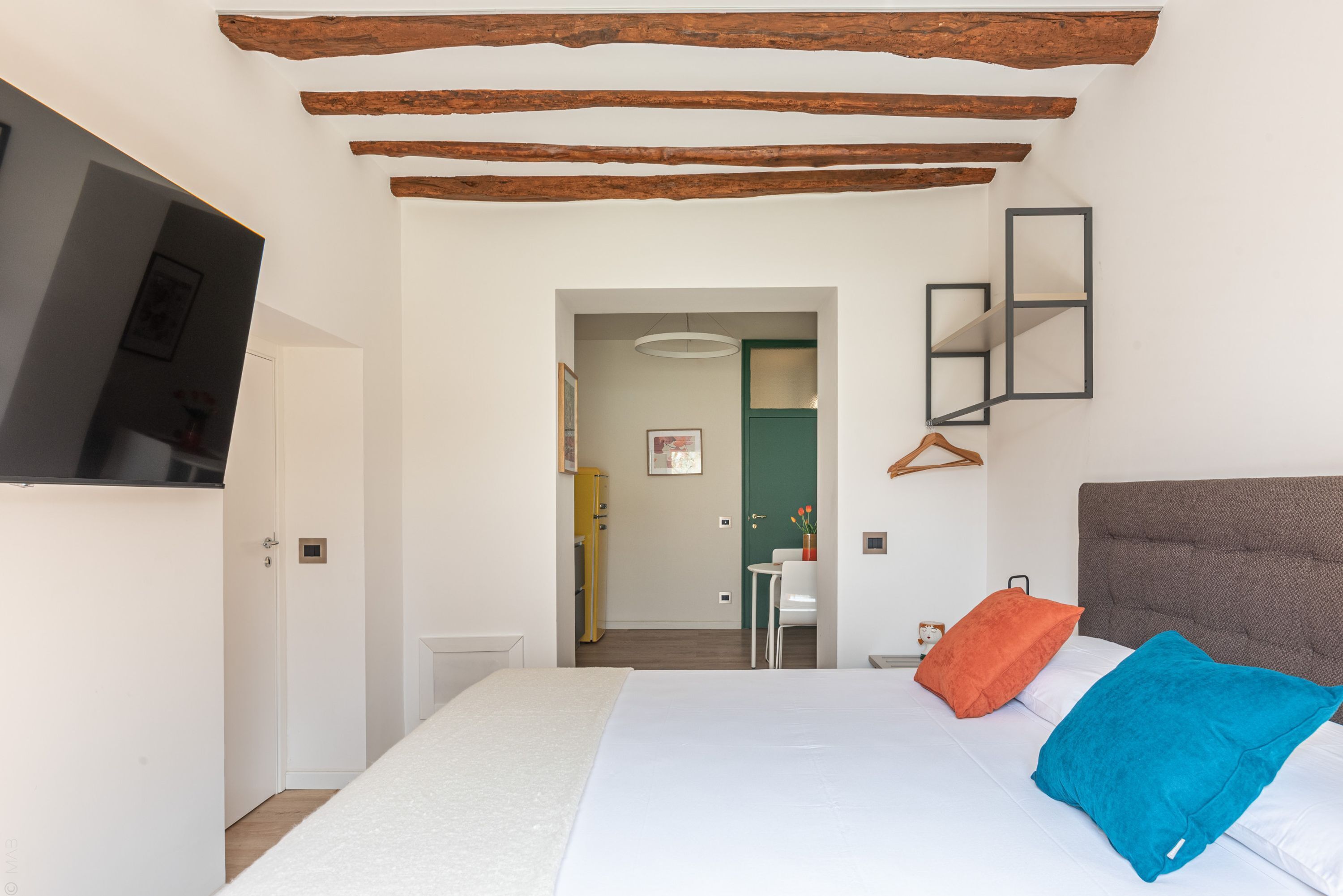 A bedroom with a bed, pillows, a television, and a wooden ceiling.