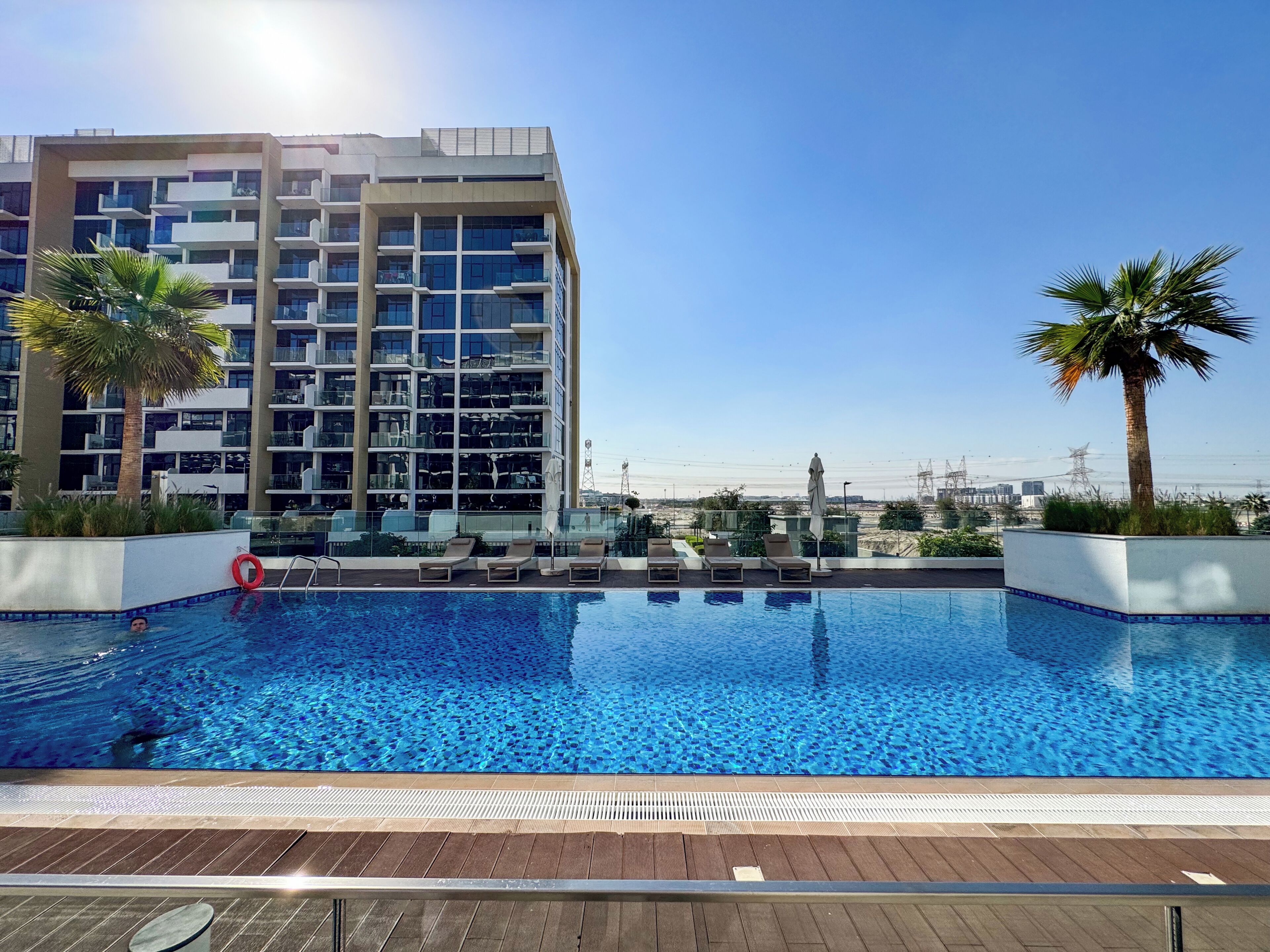 Ein modernes Hotel mit Pool auf dem Dach, Palmen und freiem Blick auf die Stadtlandschaft.