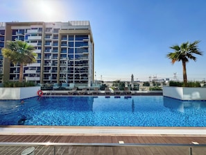 Ein modernes Hotel mit Pool auf dem Dach, Palmen und freiem Blick auf die Stadtlandschaft.